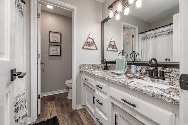 full bathroom featuring toilet, baseboards, a sink, double vanity, and wood finished floors