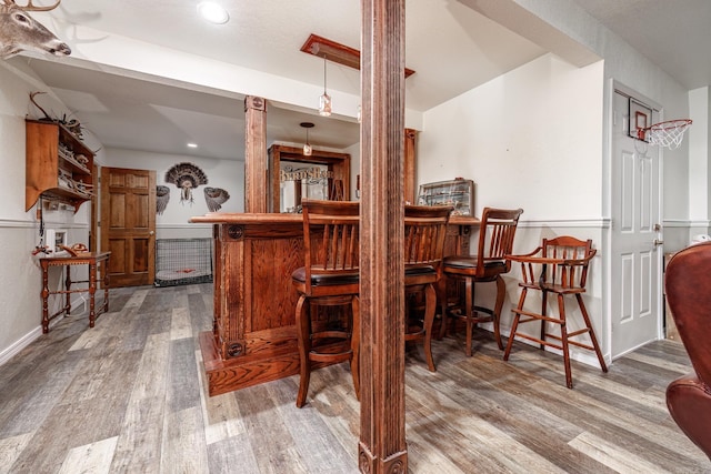bar with a bar, baseboards, wood finished floors, decorative columns, and decorative light fixtures