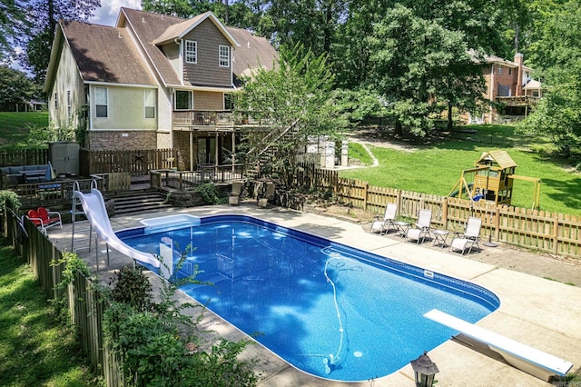 view of swimming pool with a diving board, a water slide, a wooden deck, a fenced backyard, and a playground