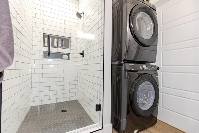 clothes washing area with wood finished floors, stacked washer / drying machine, and laundry area