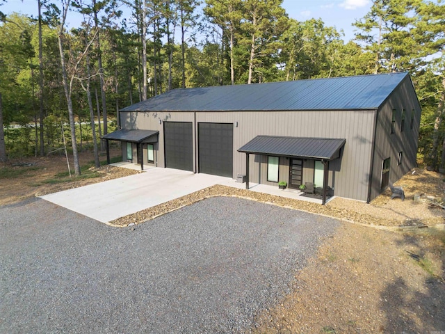 view of front of house with driveway, metal roof, a garage, and an outbuilding