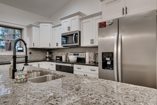 kitchen with vaulted ceiling, light stone counters, white cabinetry, stainless steel appliances, and decorative backsplash