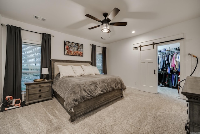 carpeted bedroom with a ceiling fan, a barn door, a walk in closet, visible vents, and recessed lighting