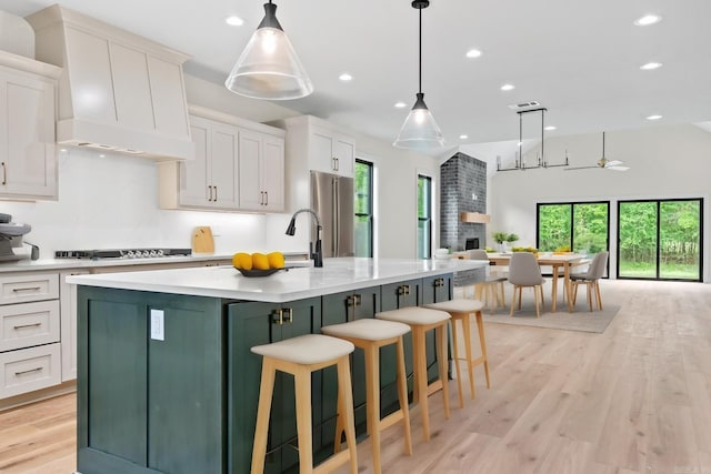 kitchen featuring light countertops, light wood-style flooring, a kitchen island with sink, open floor plan, and freestanding refrigerator