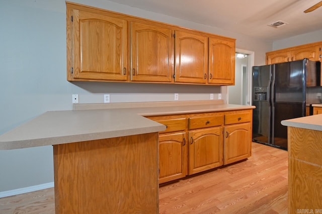kitchen featuring light wood finished floors, black fridge with ice dispenser, visible vents, and a peninsula