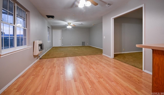 unfurnished living room with heating unit, light wood-type flooring, visible vents, and ceiling fan
