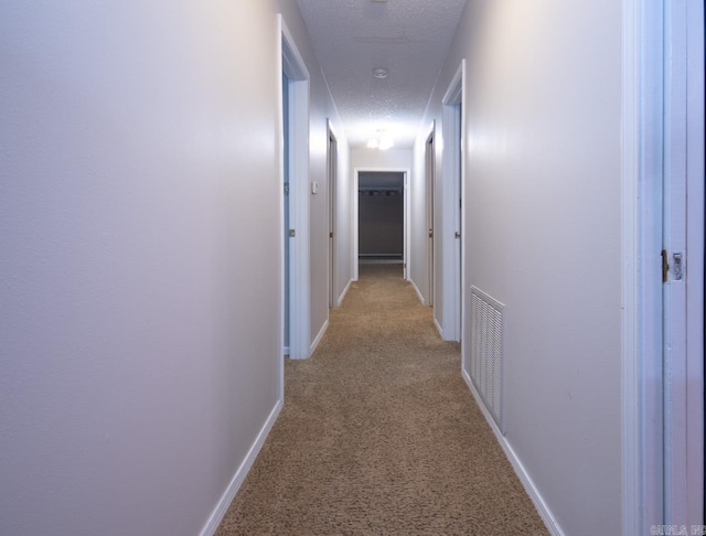 hall with light carpet, baseboards, visible vents, and a textured ceiling