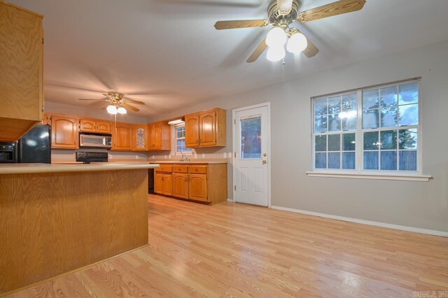 kitchen with light countertops, black refrigerator with ice dispenser, stainless steel microwave, light wood finished floors, and a ceiling fan