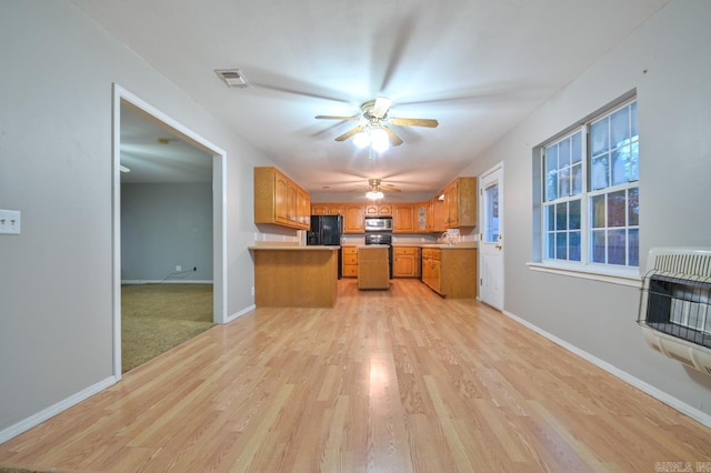 kitchen with visible vents, stainless steel microwave, heating unit, brown cabinetry, and freestanding refrigerator