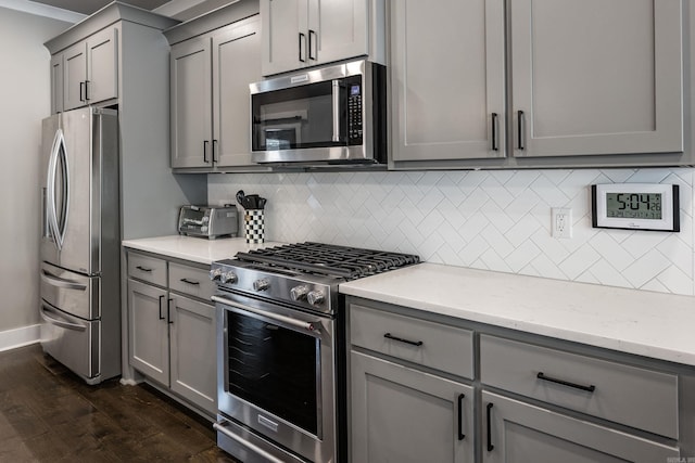kitchen featuring light stone counters, appliances with stainless steel finishes, gray cabinetry, dark wood-style floors, and decorative backsplash