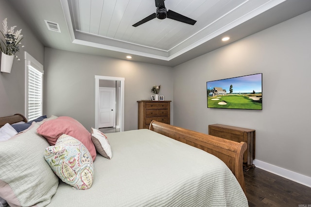 bedroom with visible vents, baseboards, a ceiling fan, dark wood-type flooring, and a tray ceiling