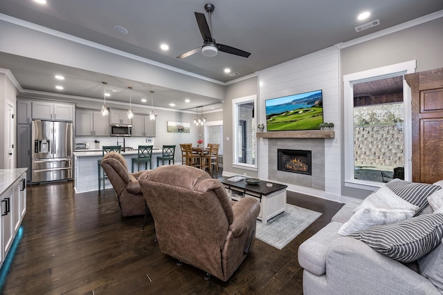 living area with dark wood finished floors, crown molding, a healthy amount of sunlight, and visible vents