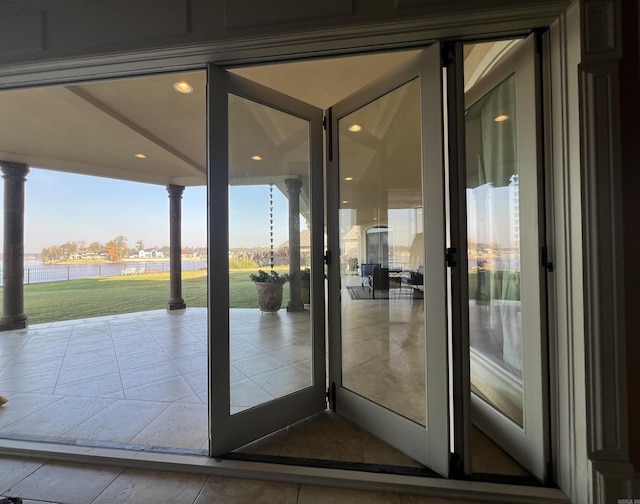 doorway with decorative columns, tile patterned flooring, and a water view