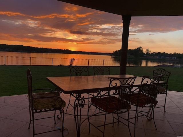patio terrace at dusk with outdoor dining area, a water view, fence, and a yard