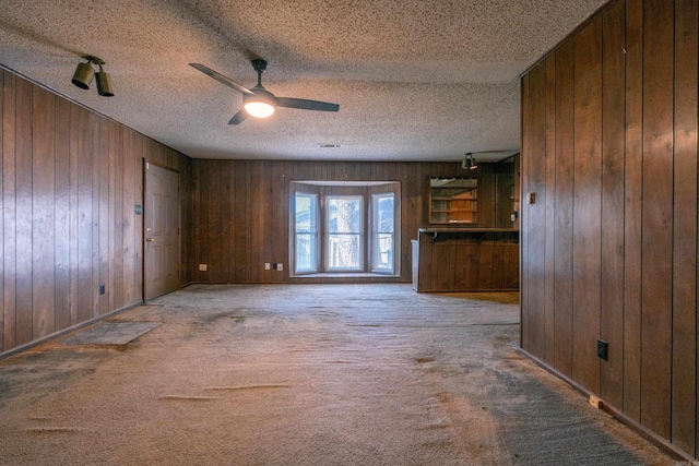 unfurnished living room featuring a ceiling fan, carpet, wooden walls, and a textured ceiling
