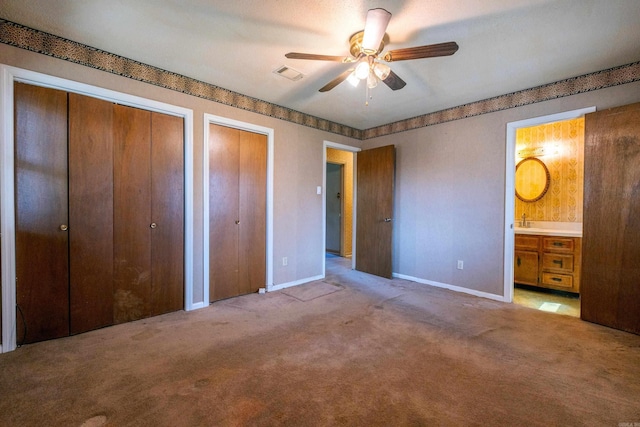 unfurnished bedroom with visible vents, carpet, two closets, a sink, and ensuite bath