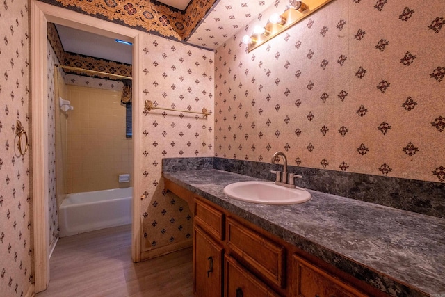 bathroom with baseboards, wallpapered walls, vanity, and wood finished floors