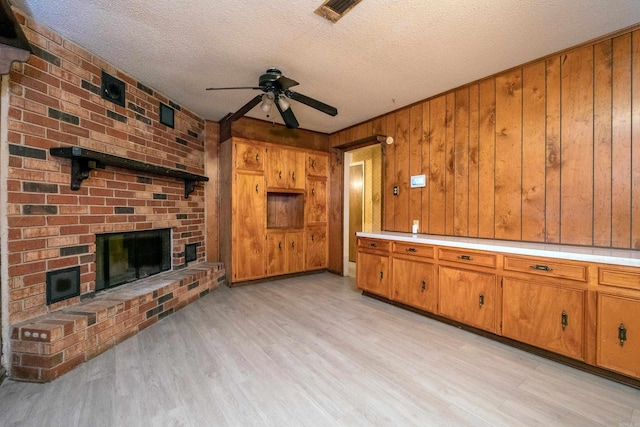 unfurnished living room featuring light wood finished floors, a brick fireplace, visible vents, and a ceiling fan
