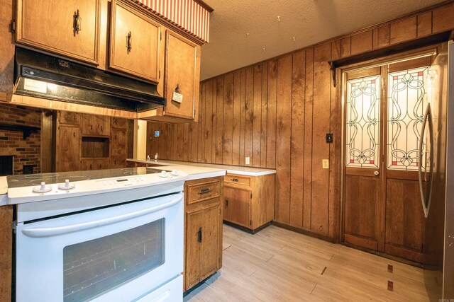 kitchen featuring freestanding refrigerator, white electric stove, wooden walls, brown cabinets, and under cabinet range hood