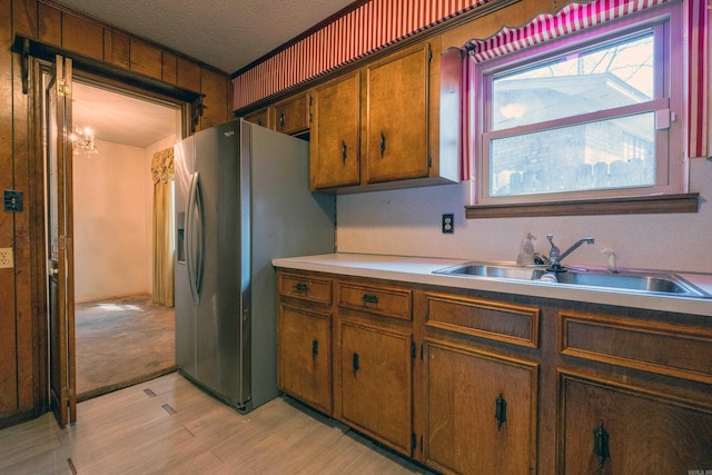 kitchen with stainless steel fridge with ice dispenser, a textured ceiling, a sink, light wood finished floors, and brown cabinetry
