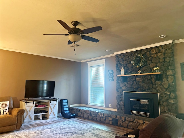 living room featuring crown molding, ceiling fan, a stone fireplace, and wood finished floors