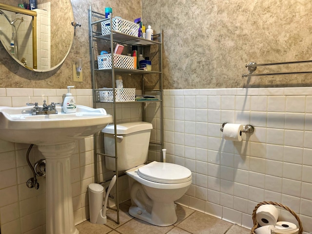 bathroom with tile patterned floors, a wainscoted wall, toilet, tile walls, and a sink