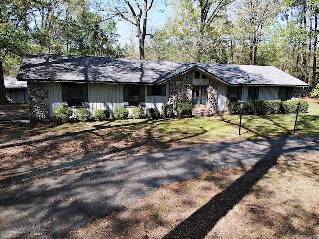 view of front facade featuring board and batten siding, stone siding, and a front lawn