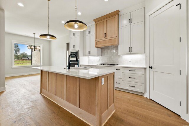 6172 Majestic Waters Dr, Alexander, AR 72002 - kitchen featuring a sink, tasteful backsplash, light countertops, an island with sink, and light wood-style floors