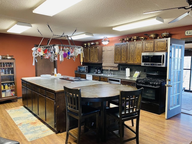 kitchen featuring tasteful backsplash, stainless steel microwave, black range with gas cooktop, and light wood-style floors