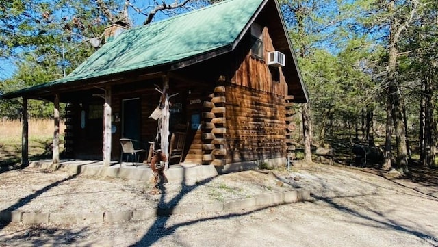 view of side of property featuring a porch, log exterior, metal roof, and a chimney