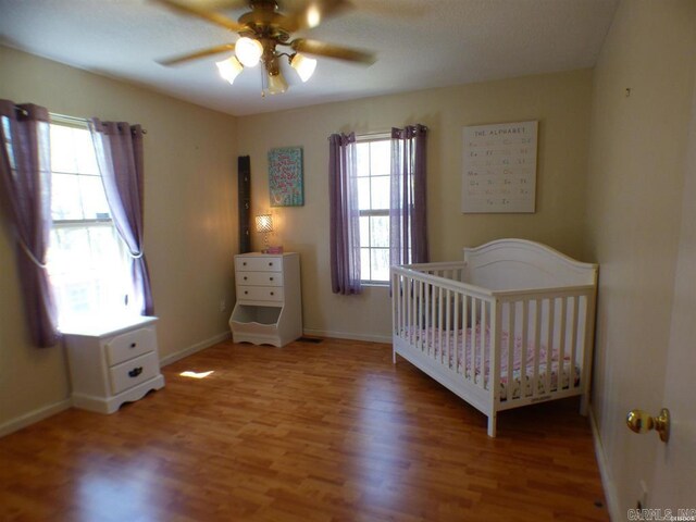 302 Veranda, Pearcy, AR 71964 - unfurnished bedroom featuring a nursery area, baseboards, a ceiling fan, and light wood-style floors