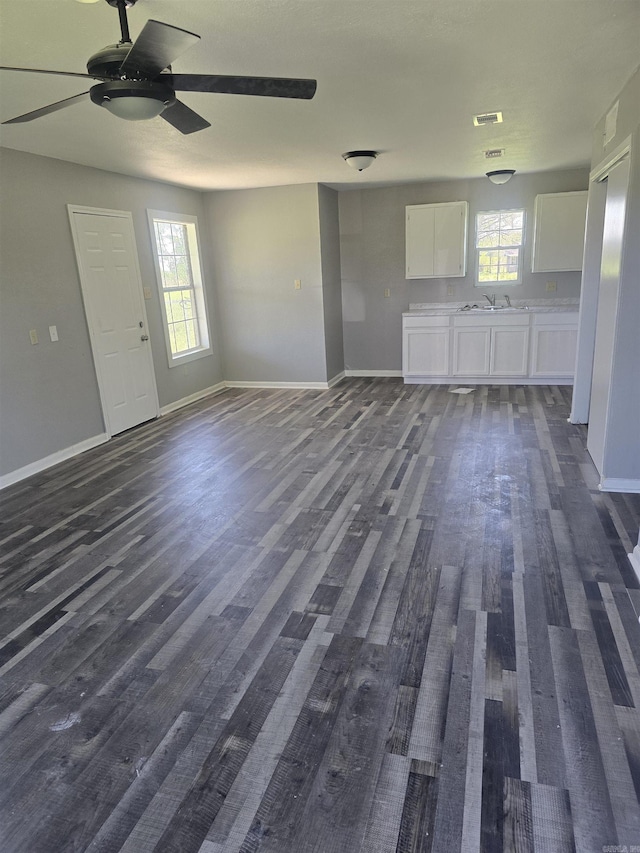 unfurnished living room featuring baseboards, a ceiling fan, plenty of natural light, and dark wood-style floors