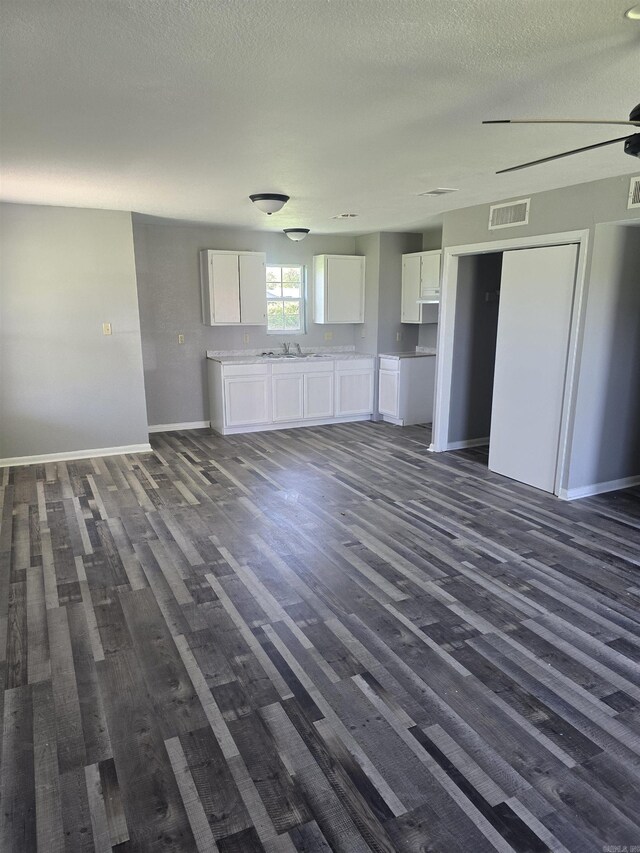 unfurnished living room featuring dark wood finished floors, a textured ceiling, visible vents, a sink, and baseboards