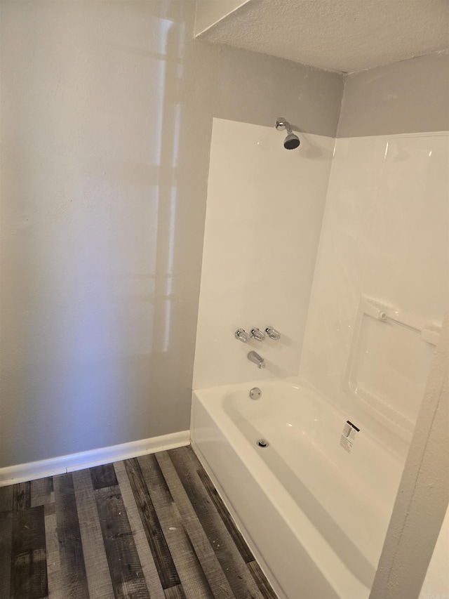 bathroom featuring shower / washtub combination, a textured ceiling, baseboards, and wood finished floors