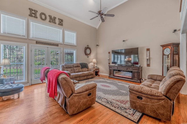living room with high vaulted ceiling, ceiling fan, light wood-type flooring, ornamental molding, and baseboards
