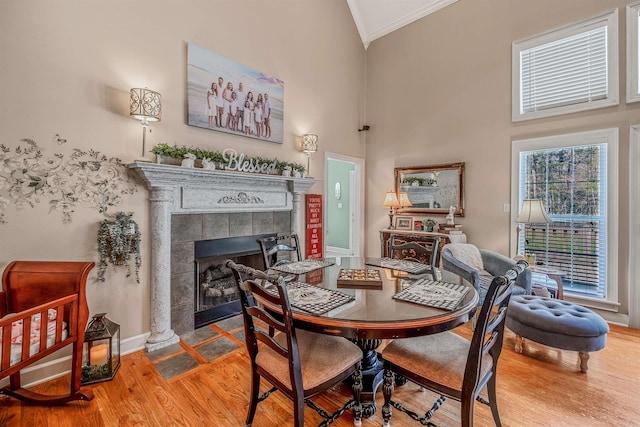 dining room with baseboards, a high ceiling, crown molding, wood finished floors, and a tile fireplace