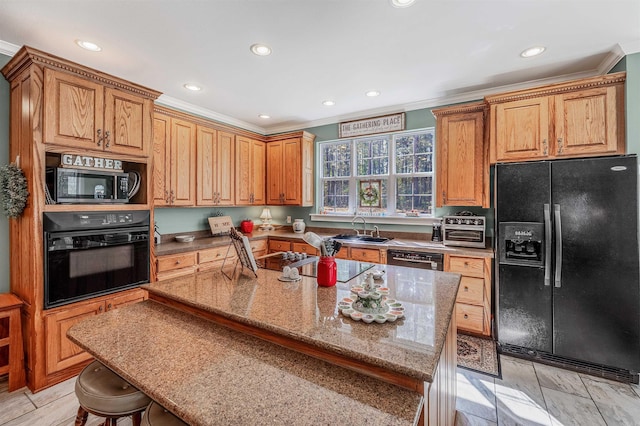 kitchen with light stone counters, a kitchen island, black appliances, a kitchen bar, and a sink