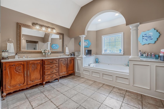 full bath with a bath, a sink, ornate columns, double vanity, and vaulted ceiling