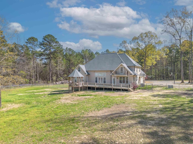 back of property featuring roof with shingles, a view of trees, a deck, fence, and a lawn