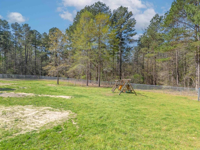 view of yard featuring a wooded view, a fenced backyard, and a playground