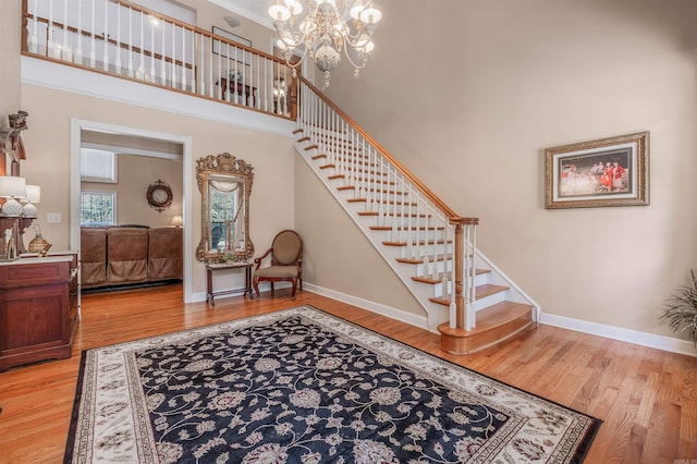 staircase featuring a notable chandelier, a towering ceiling, baseboards, and wood finished floors