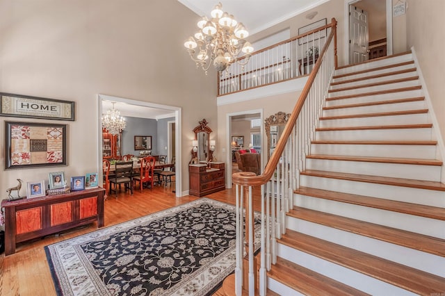 staircase featuring a chandelier, crown molding, wood finished floors, and a high ceiling