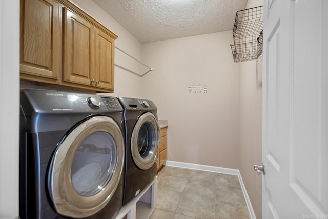 laundry area featuring baseboards, a textured ceiling, cabinet space, washer and clothes dryer, and light tile patterned flooring