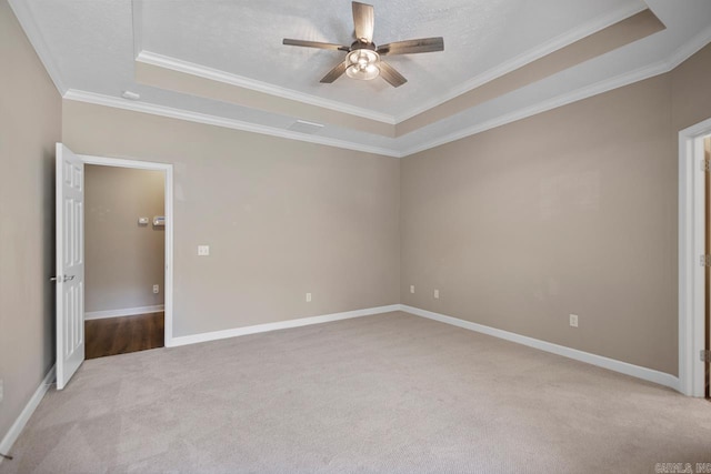 unfurnished bedroom with baseboards, a textured ceiling, crown molding, a raised ceiling, and light colored carpet