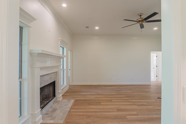 unfurnished living room featuring light wood-type flooring, ceiling fan, a tiled fireplace, and ornamental molding