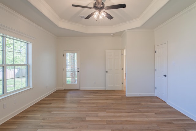 spare room featuring baseboards, ornamental molding, a tray ceiling, ceiling fan, and light wood finished floors