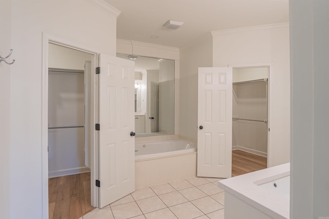 full bath with a garden tub, vanity, ornamental molding, tile patterned flooring, and a walk in closet