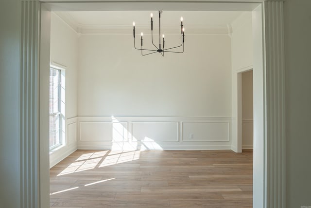 unfurnished dining area featuring ornamental molding, light wood-style flooring, a chandelier, and wainscoting