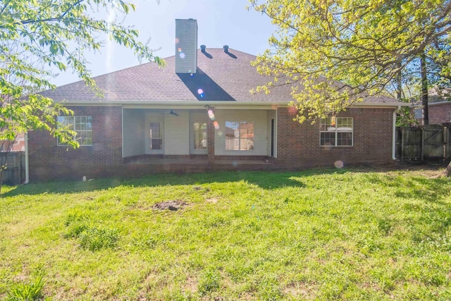 back of property with a lawn, a chimney, fence, brick siding, and roof with shingles
