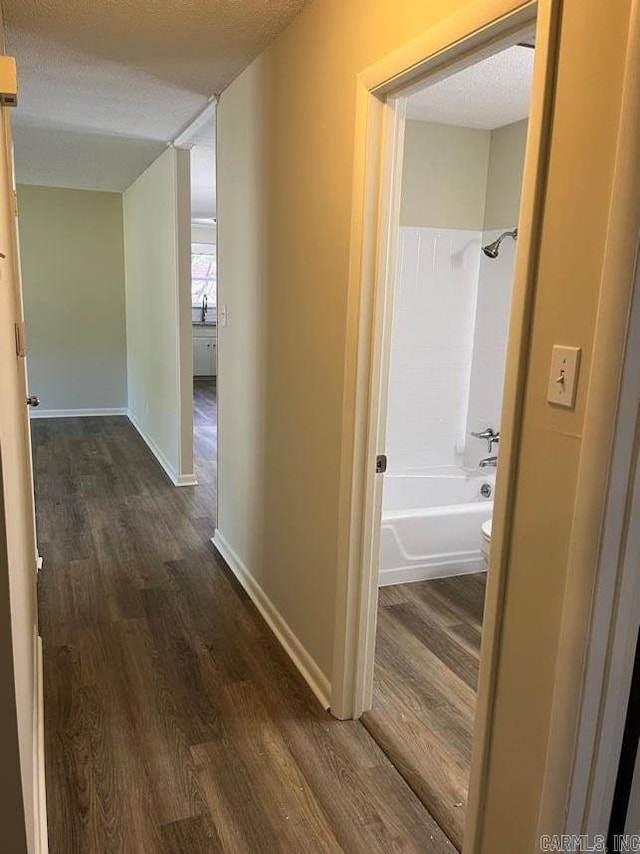 corridor featuring a textured ceiling, dark wood-style flooring, and baseboards